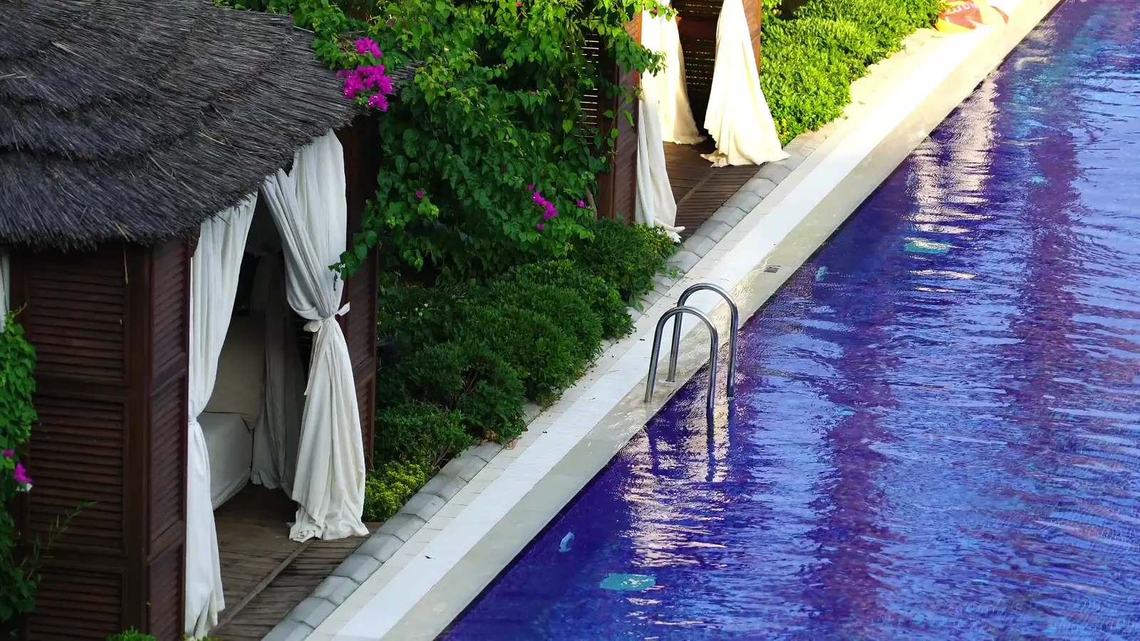 Piscina lineal junto a cabañas con cortinas blancas